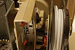 When working on this area of the projector, it is easiest to remove the front cover. The cover is held in place with three bolts. This is the middle bolt when looking at the back of the projector, it also helps hold the film transport mechanism in place