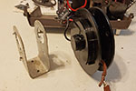 It can be a bit of a struggle but remove the mechanism from its support. Pay attention to how the various components are placed and be careful not to strip any insulation from any of the wires. The tension to rewind the main electrical cord is provided by about 10ft of spring steel that is wound inside the mechanism, be careful not to let the mechanism come apart yet.